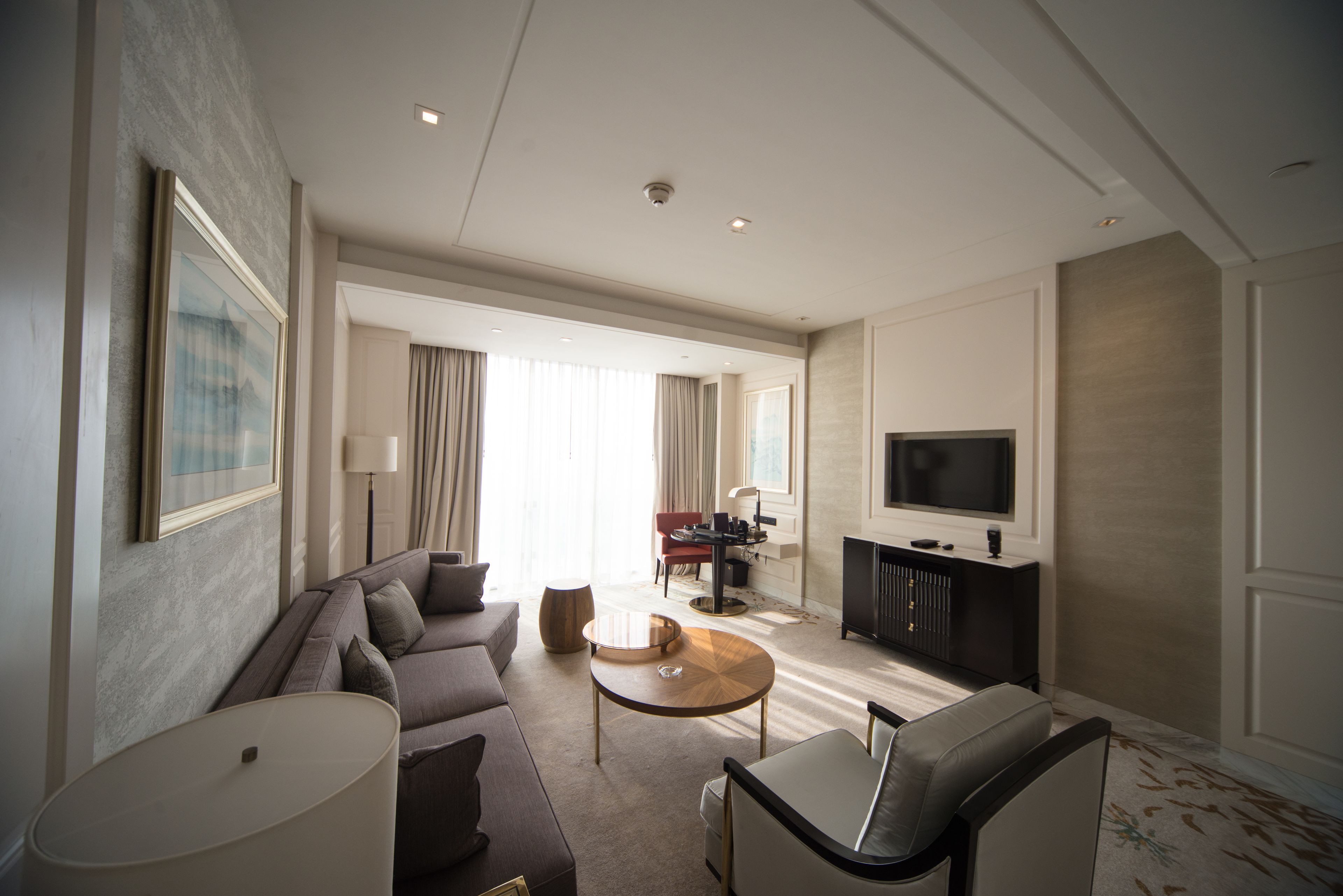 Un moderno salón de hotel con un sofá, un sillón, una mesa de centro y un televisor de pantalla plana.