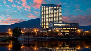 Un hôtel moderne avec une piscine dont la surface reflète l’environnement, entouré d’arbres et adossé à une montagne.