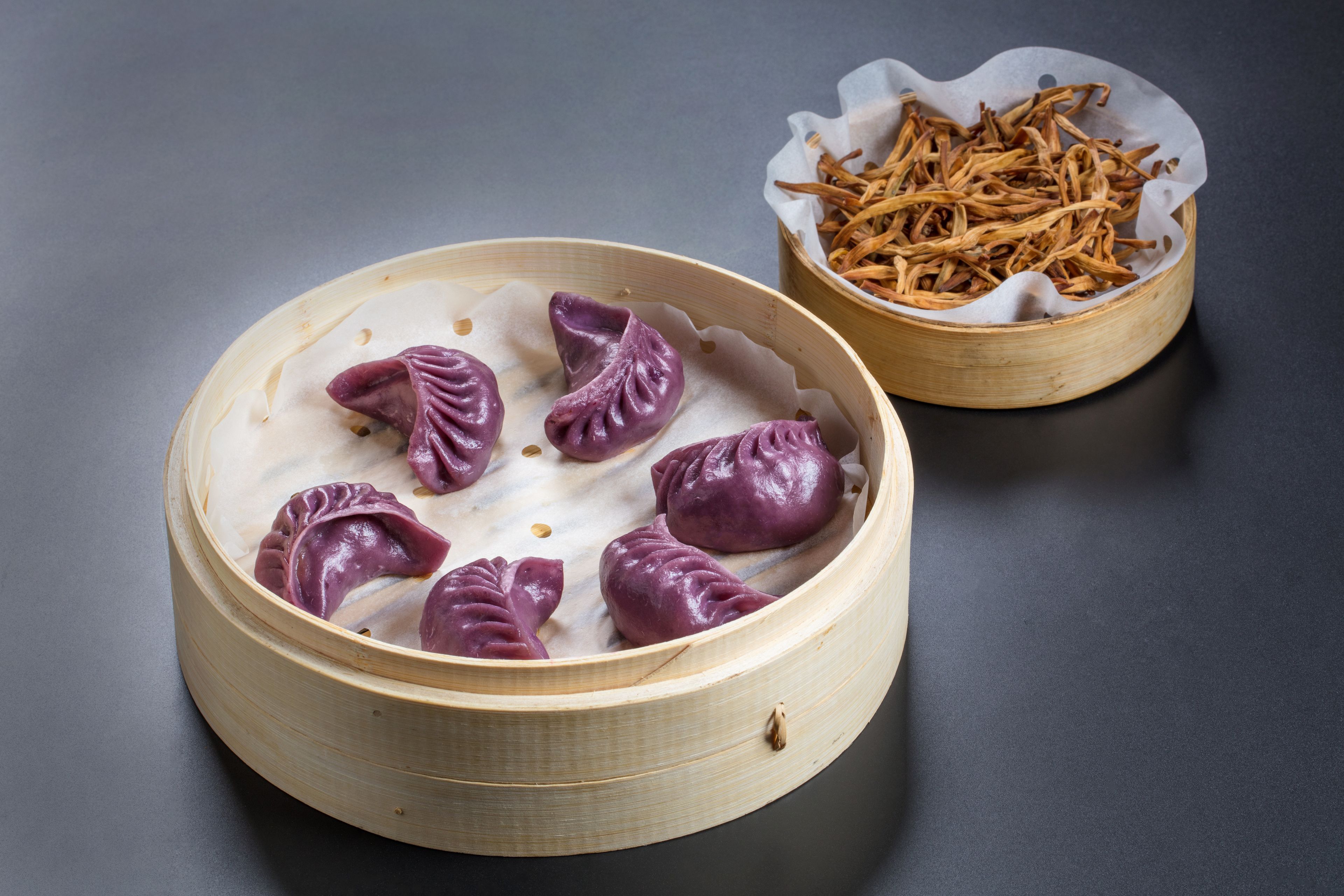 Een bamboestoommandje met paarse dumplings en een kleine schaal gedroogde theebladeren.