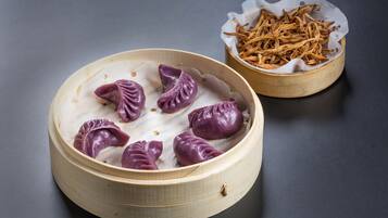 Een bamboestoommandje met paarse dumplings en een kleine schaal gedroogde theebladeren.