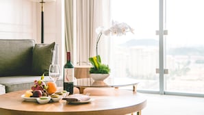 Une table ronde avec une bouteille de vin, un saladier de fruits et une orchidée blanche.