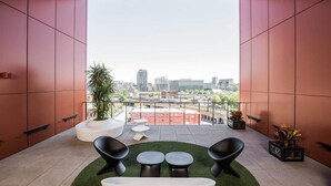 A modern balcony with a city view, featuring a white sofa, two black chairs, a small table, and a potted plant. - Hôtel Alt Montréal (Montreal)