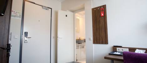A hotel room with a bed, a desk with a laptop, a shower, and a bathroom.