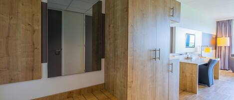 A modern hotel room with wooden furniture, a desk, and a large mirror.