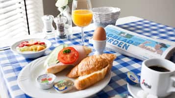 Una mesa de desayuno con mantel a cuadros, un croissant, un vaso de jugo de naranja, un periódico y una taza de café.