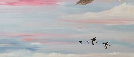 A landscape painting of ducks flying over a field of cows.