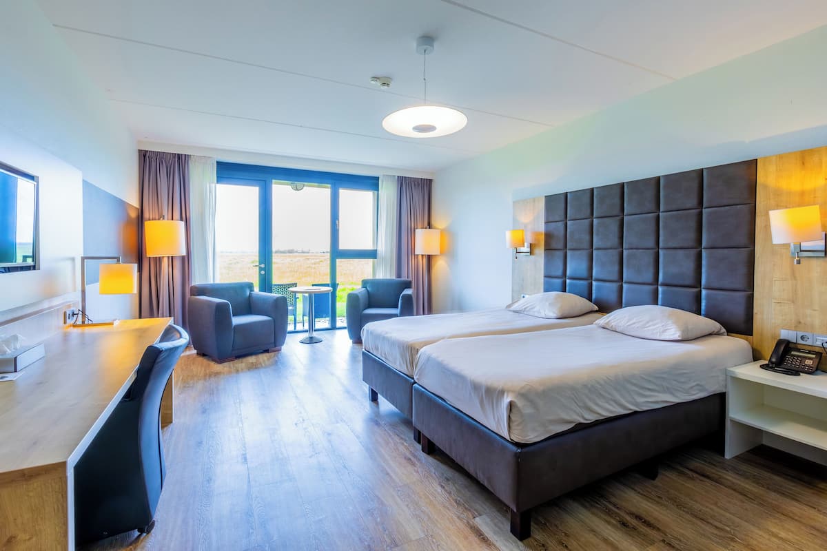 A hotel room with a large bed, a desk, a chair, and a view of the outdoors.