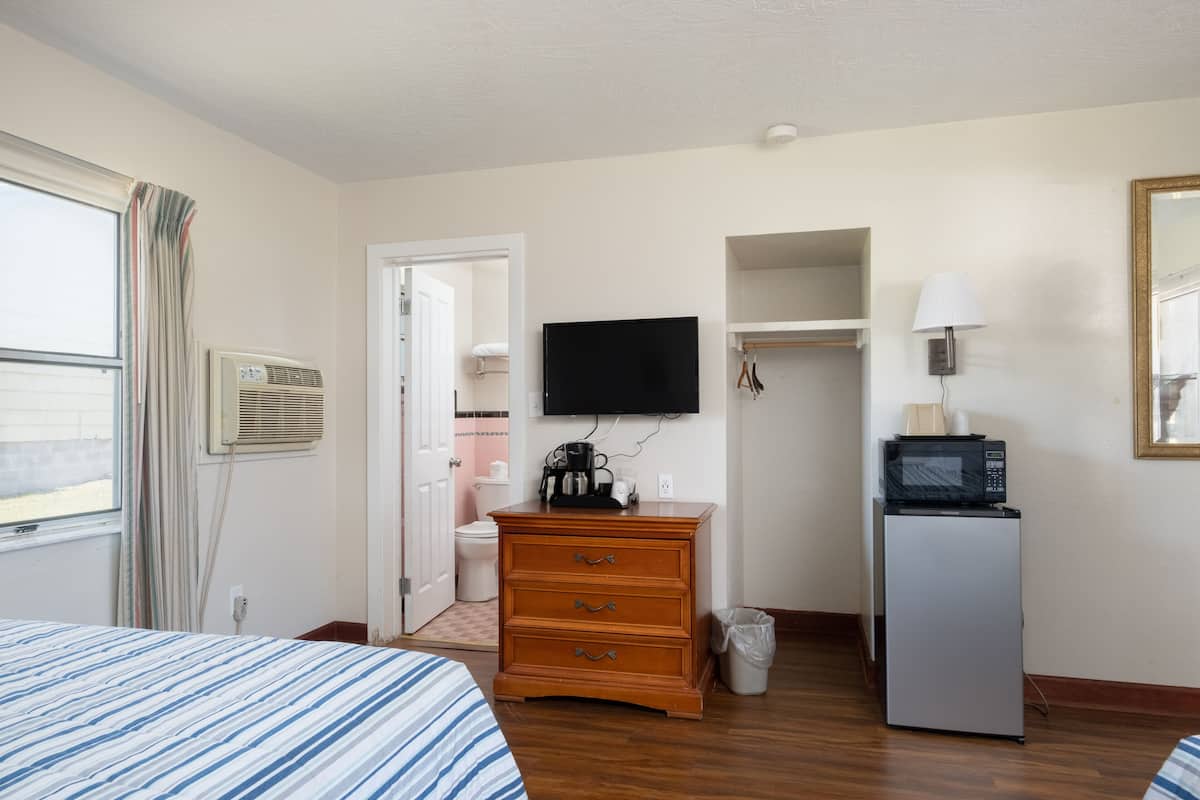 A hotel room with a bed, a dresser, a television, a microwave, and a trash can.
