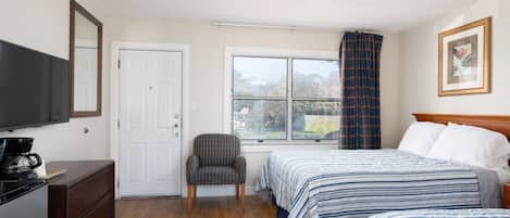 Een hotelkamer met een bed, een stoel, een televisie en een raam met gordijnen.
