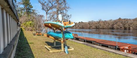 A lakeside setting with kayaks and a paddleboard, a wooden dock, and a grassy area.