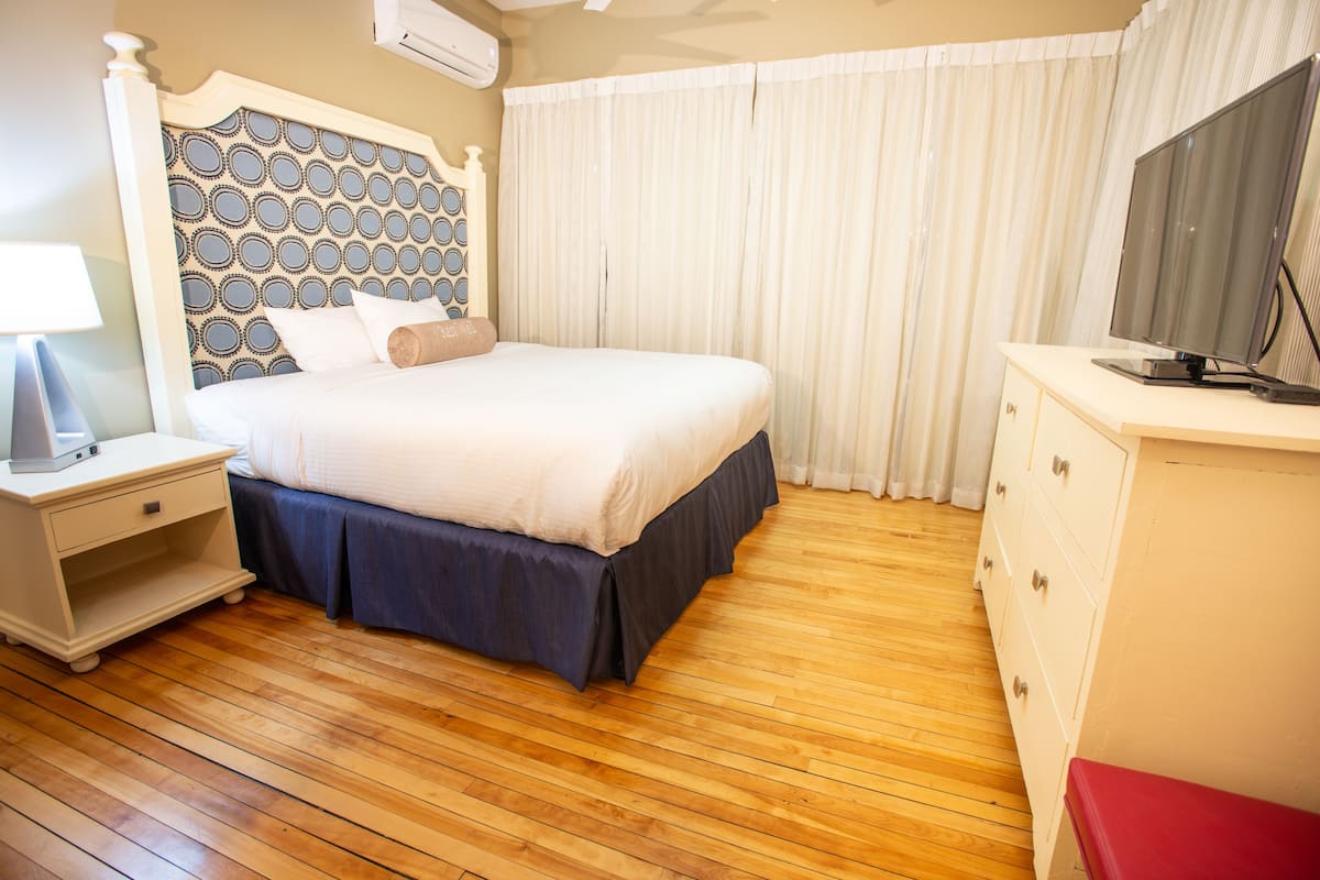 A neatly arranged bedroom with a bed, bedside table, and a TV on a dresser.