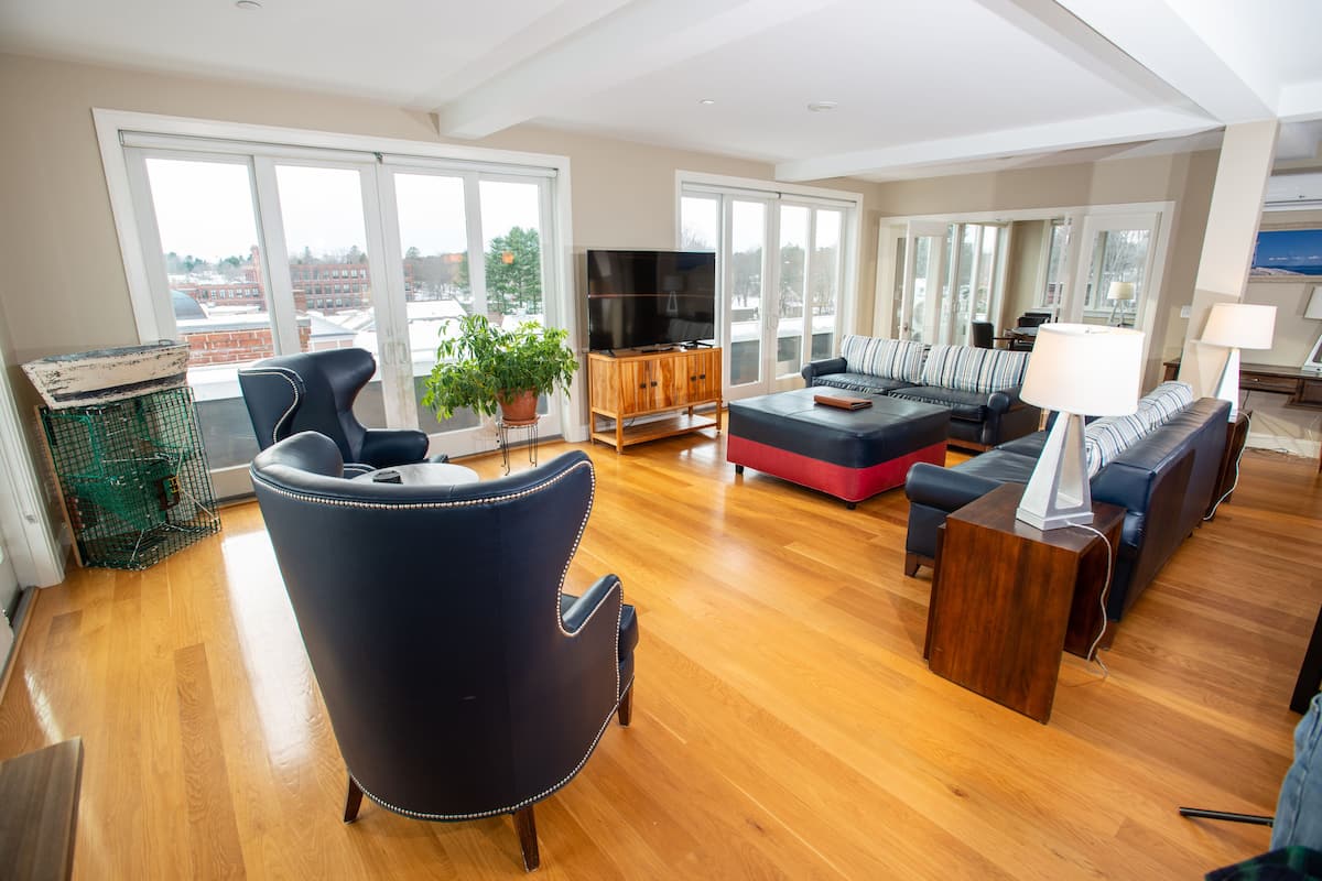 A spacious living room with a large TV, comfortable seating, and a view through large windows.