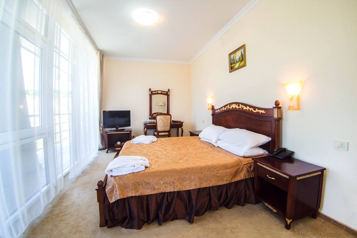 Ein Hotelzimmer mit einem großen Bett, einem Schreibtisch, einem Stuhl, einem Fernseher und einem Nachttisch mit einer Lampe.