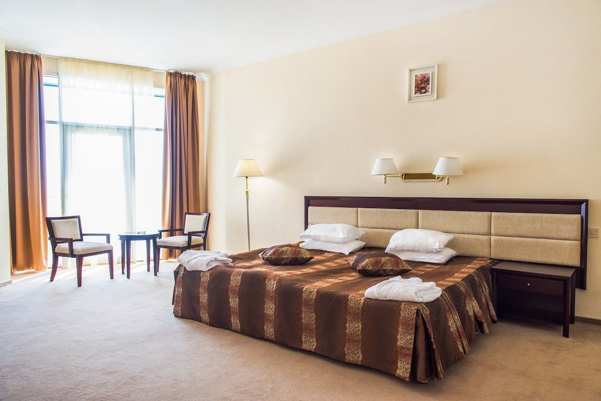 Ein Hotelzimmer mit einem großen Bett, zwei Sessel, einem kleinen Tisch und einem Nachttisch.
