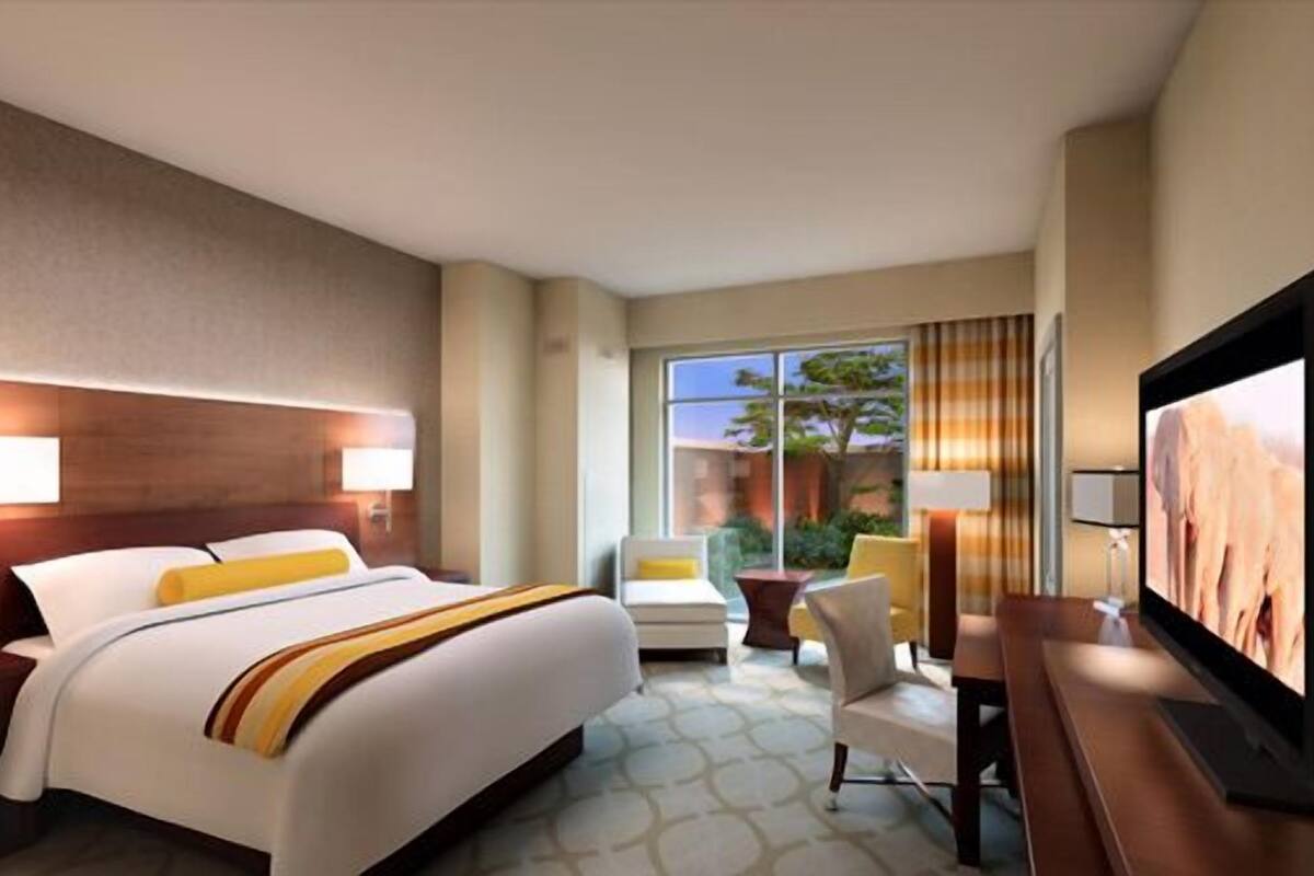 Ein Hotelzimmer mit einem großen Bett, zwei Nachttischen, einem Fernseher und Blick ins Freie.