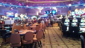 A bustling casino interior with multiple gaming tables and chairs, neon signs, and a patterned floor.