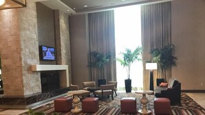 A spacious lobby with a stone fireplace, comfortable seating, large windows, and potted plants.