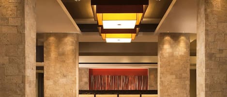 A spacious lobby with a patterned floor, a central red accent wall, and a modern ceiling light fixture.