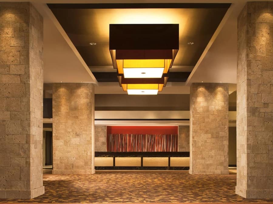 Um lobby espaçoso com piso estampado, uma parede central em vermelho e um moderno lustre.