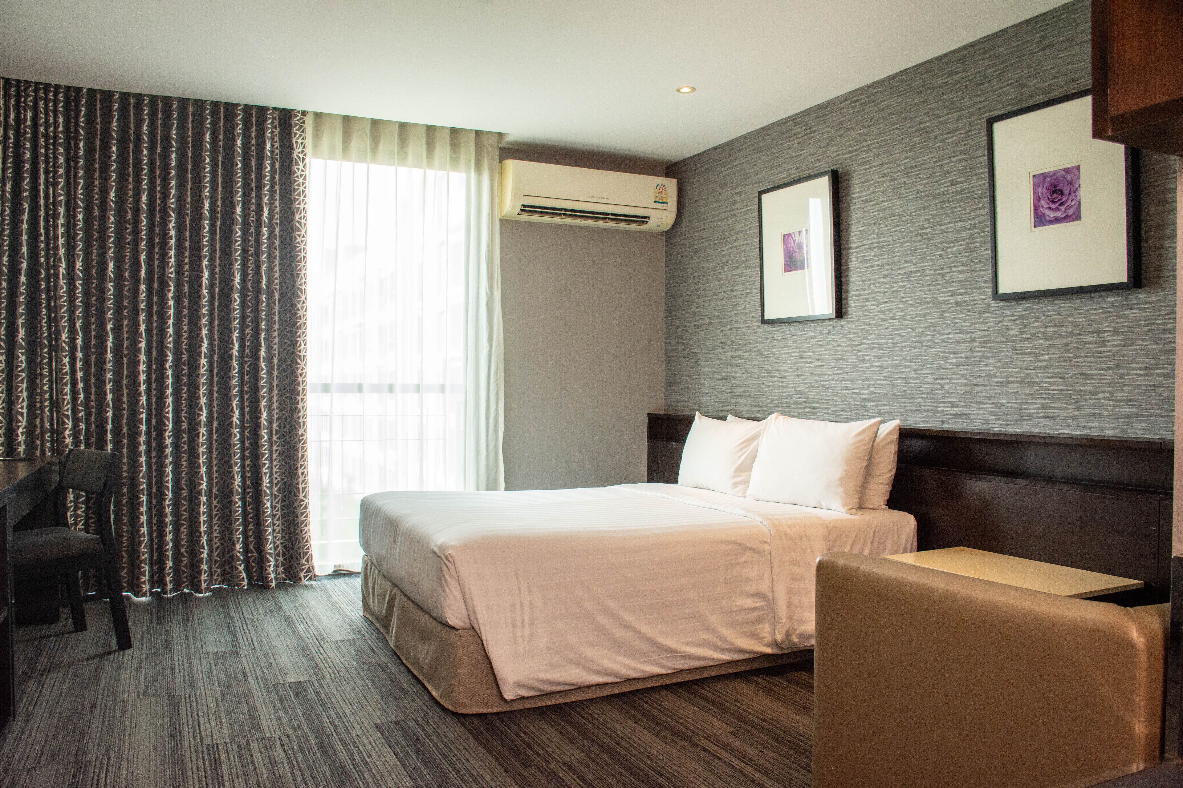 A hotel room with a bed, a desk, a chair, an air conditioner, and a window with curtains.