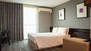 A hotel room with a bed, a desk, a chair, an air conditioner, and a window with curtains.