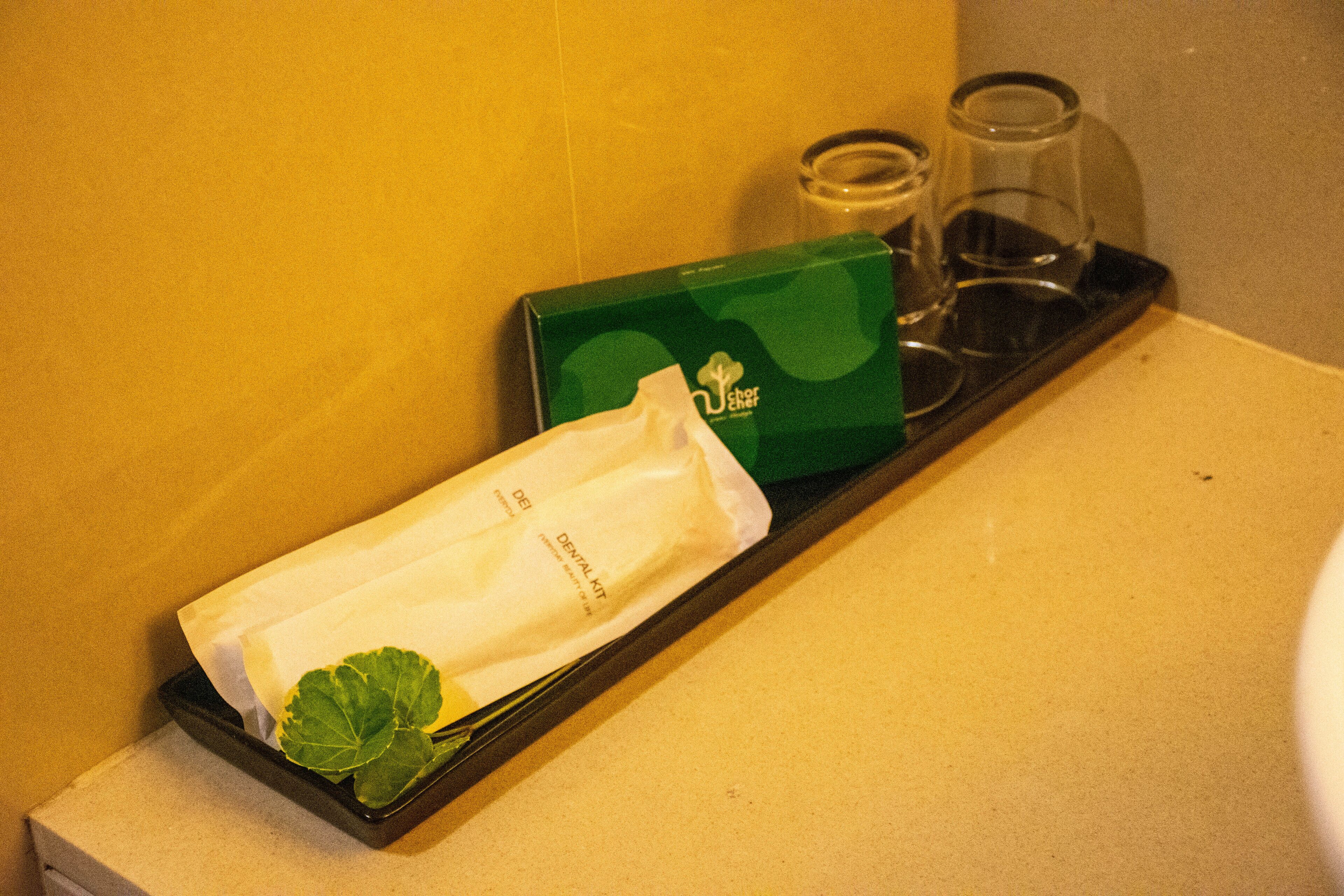 Una bandeja con una caja verde etiquetada 'Jaber', un pañuelo blanco y dos vasos transparentes sobre una encimera.