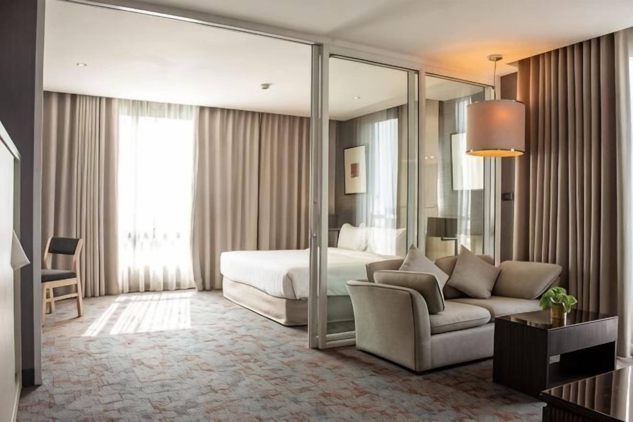 A hotel room with a bed, a sofa, a coffee table, a chair, and a large mirror.