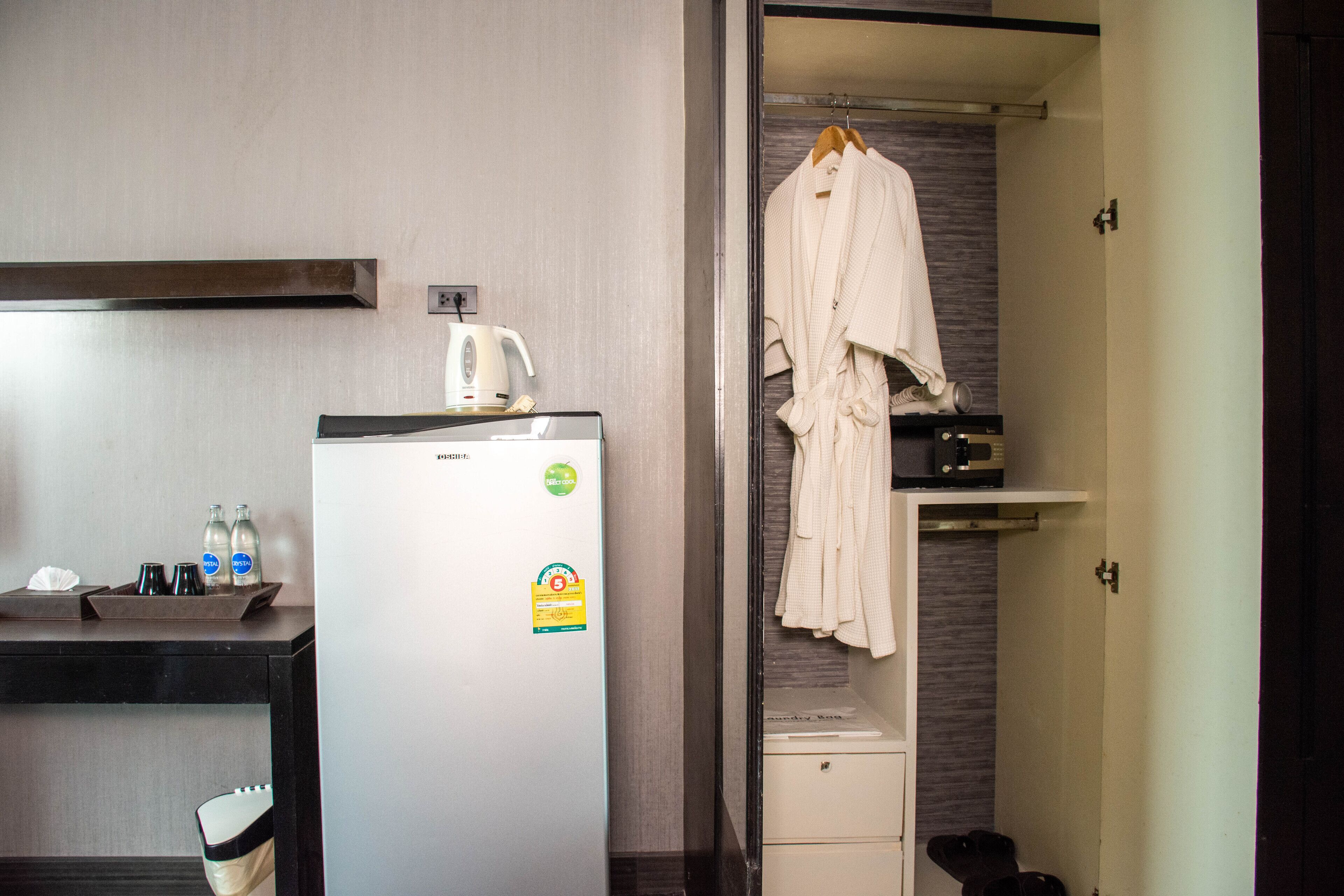 Habitación de hotel con refrigerador, cafetera y bata colgada en un perchero.