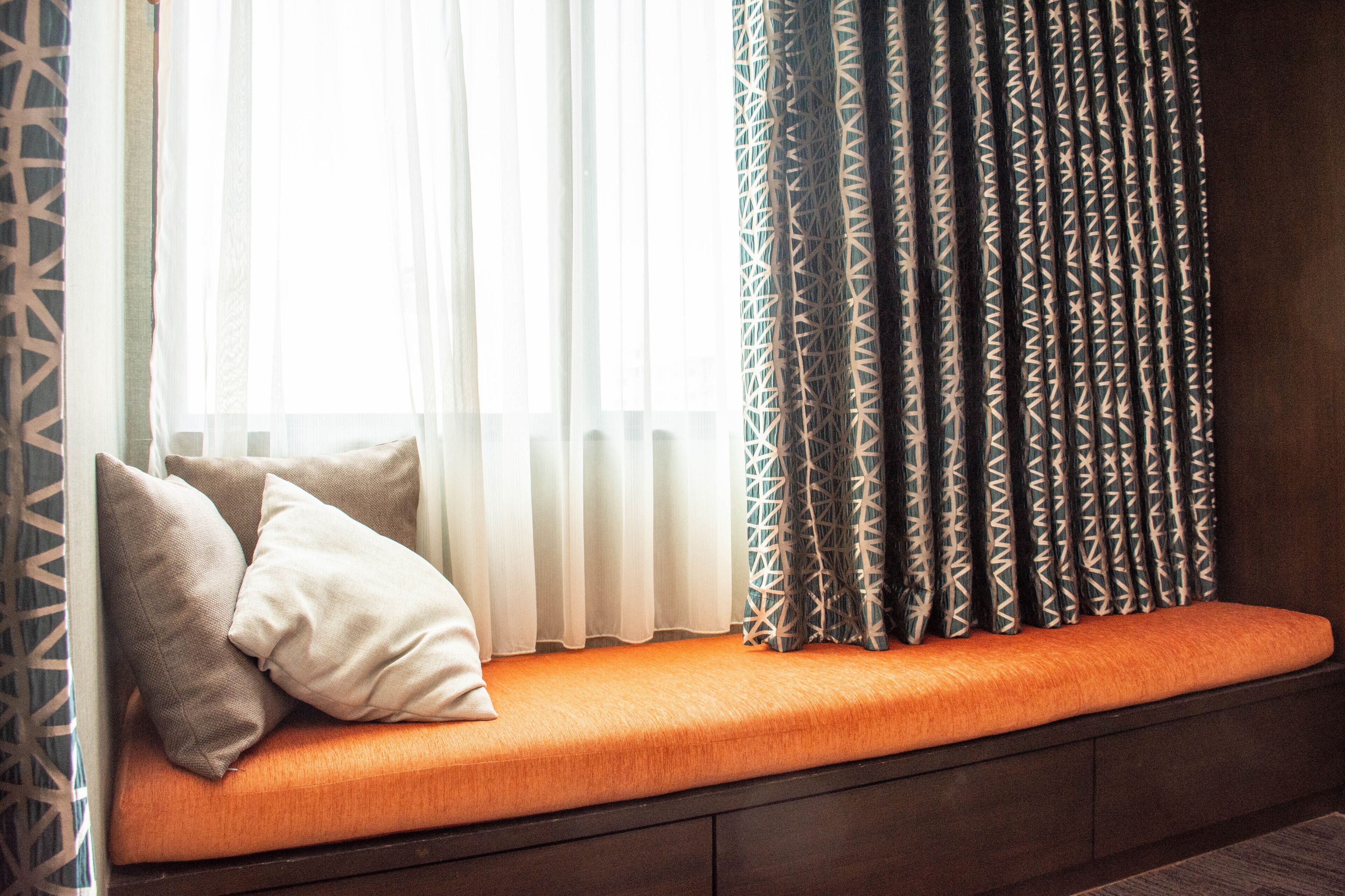 A window seat with cushions, a patterned curtain, and a view of the outside.