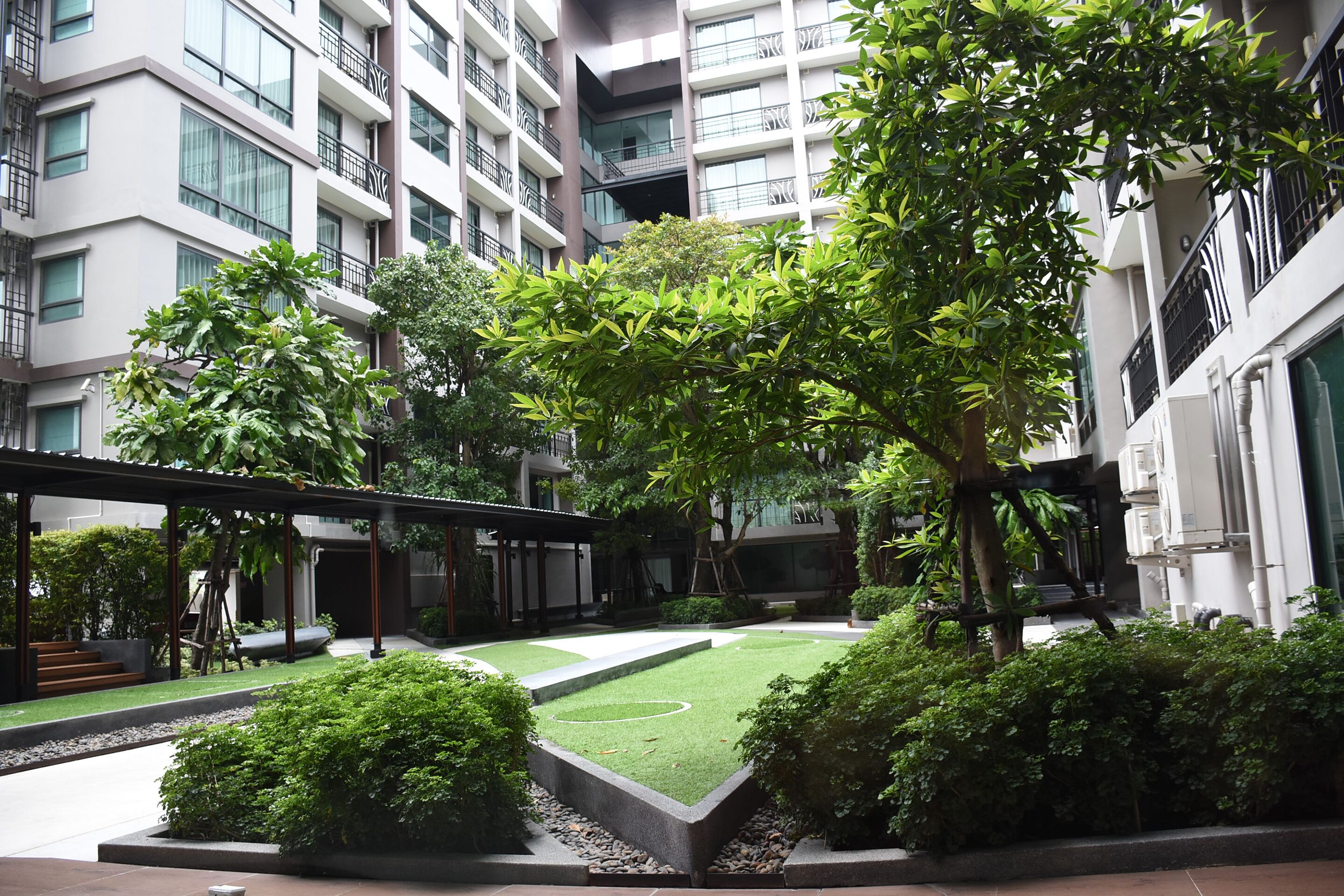 Un edificio moderno con varios pisos, grandes ventanales y balcones. Cuenta con un patio cuidado con césped, arbustos y árboles.
