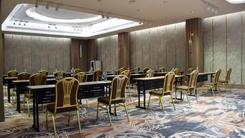 A conference room with rows of tables and chairs, a large ceiling light, and patterned walls.