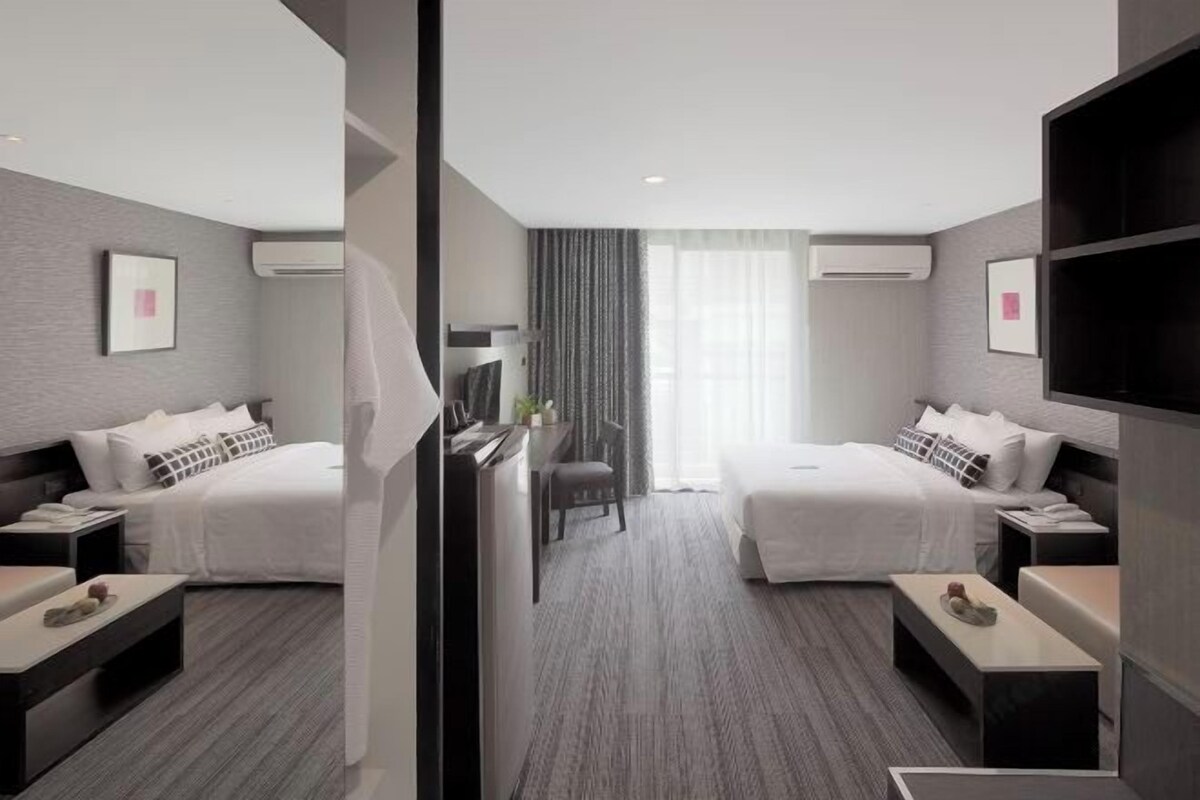 A modern hotel room with two beds, a desk, a chair, and a TV.