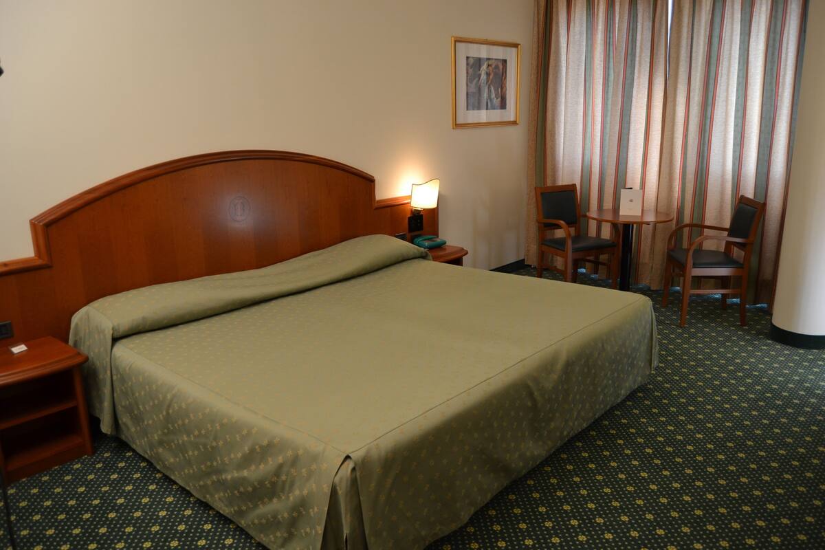 A hotel room with a large bed, a nightstand, a lamp, two chairs, and a framed picture on the wall.