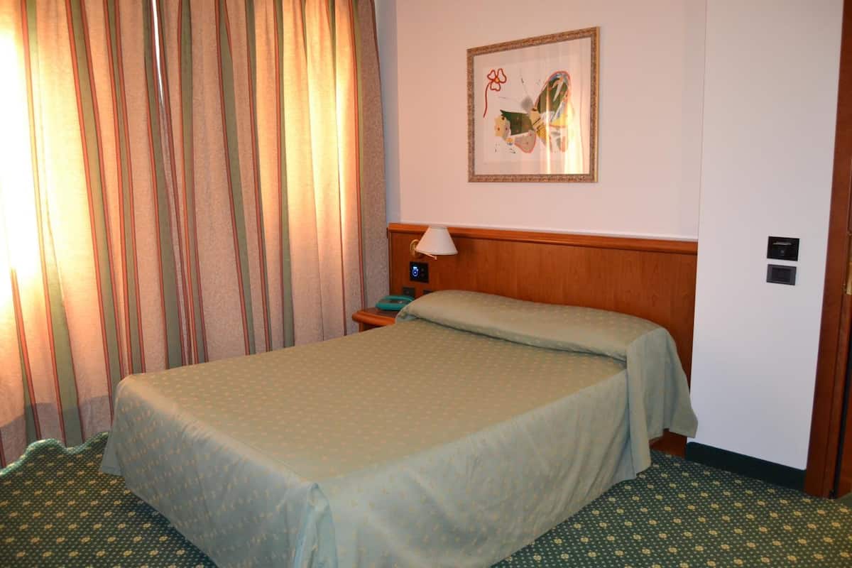 A hotel room with a bed, a nightstand, a lamp, a painting on the wall, and a curtain.