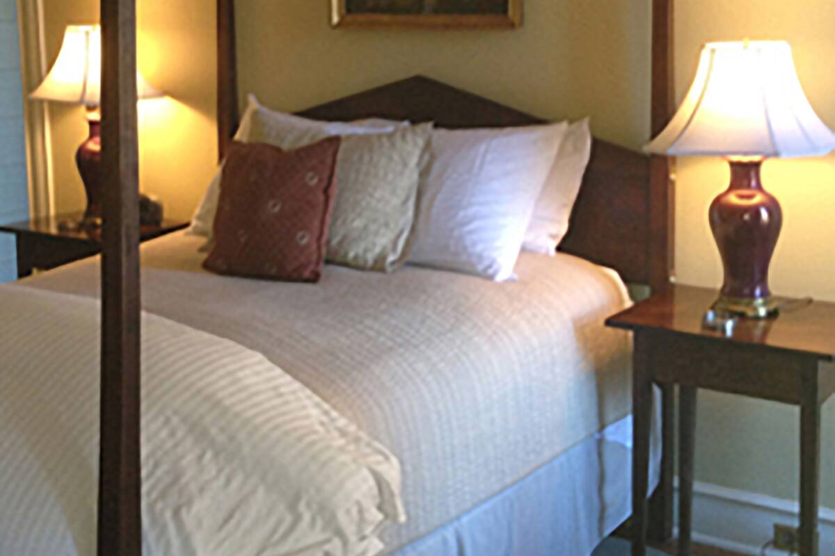 A neatly made bed with white linens and a red pillow, flanked by two bedside lamps on wooden nightstands.