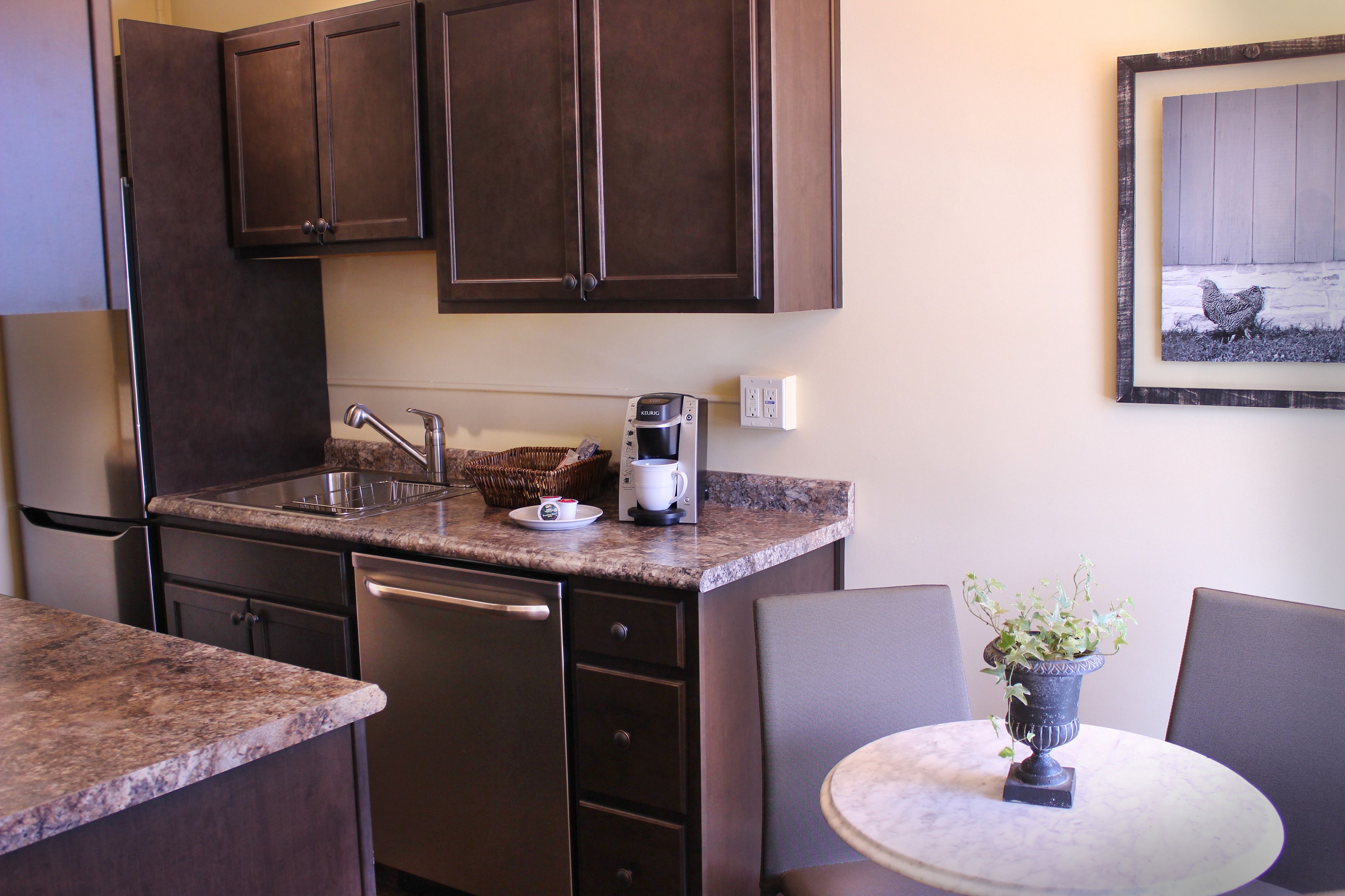 A compact kitchen with dark wooden cabinets, a built-in dishwasher, a coffee maker, and a small table with a potted plant.
