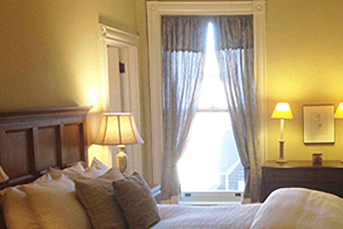 A hotel room with a large bed, two bedside lamps, a window with curtains, and a wooden headboard.