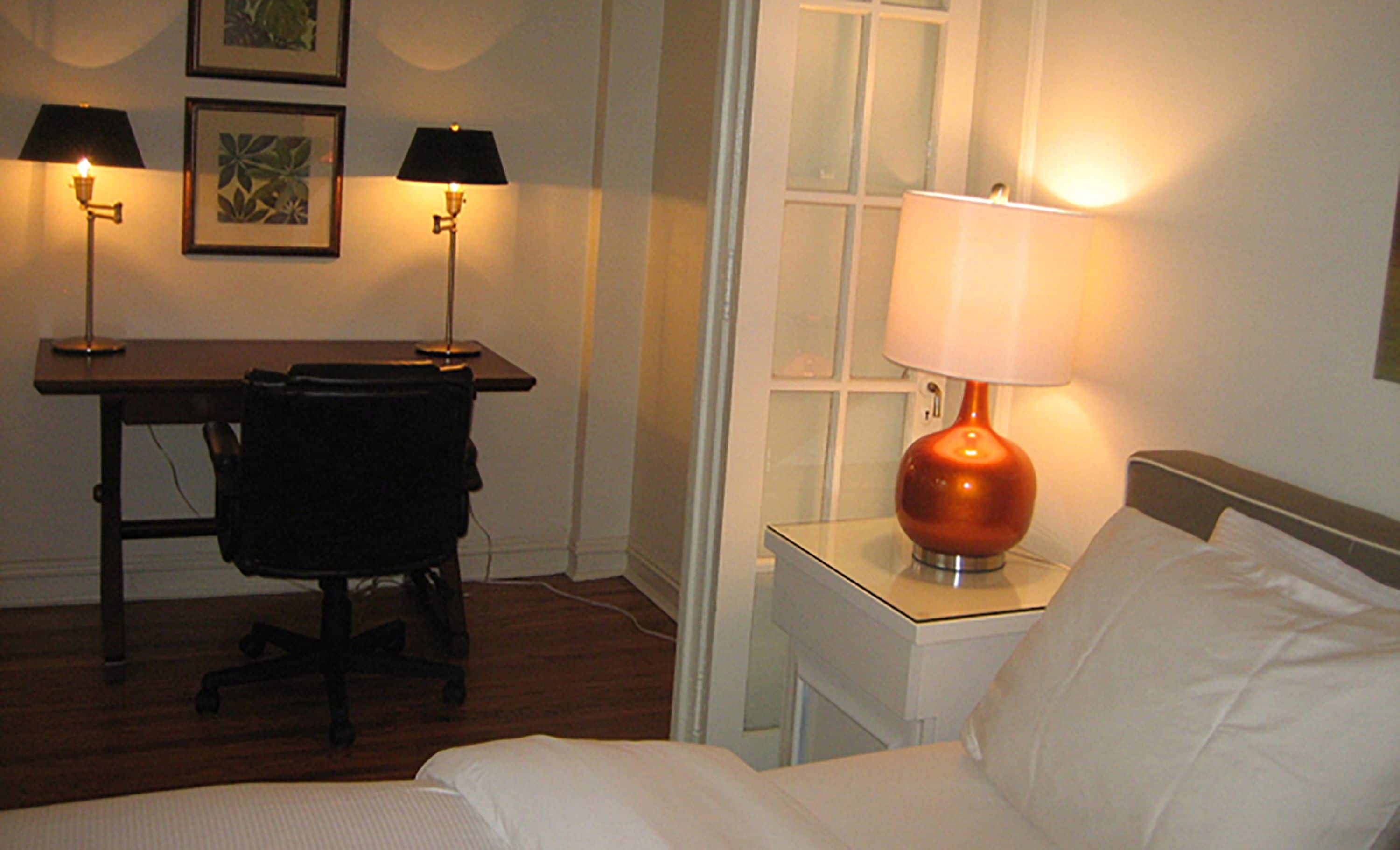A hotel room with a bed, a desk, two lamps, and a chair.