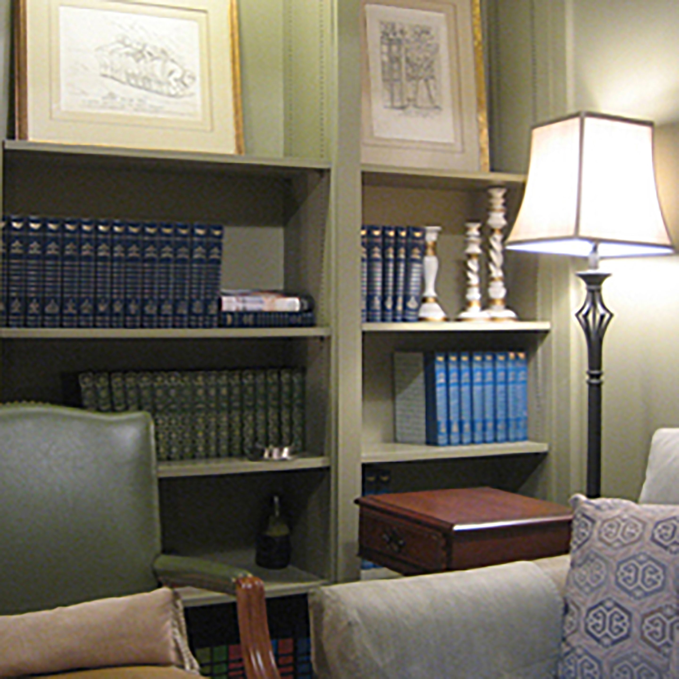 A room with a bookshelf filled with books, a lamp, a chair, and a small table.