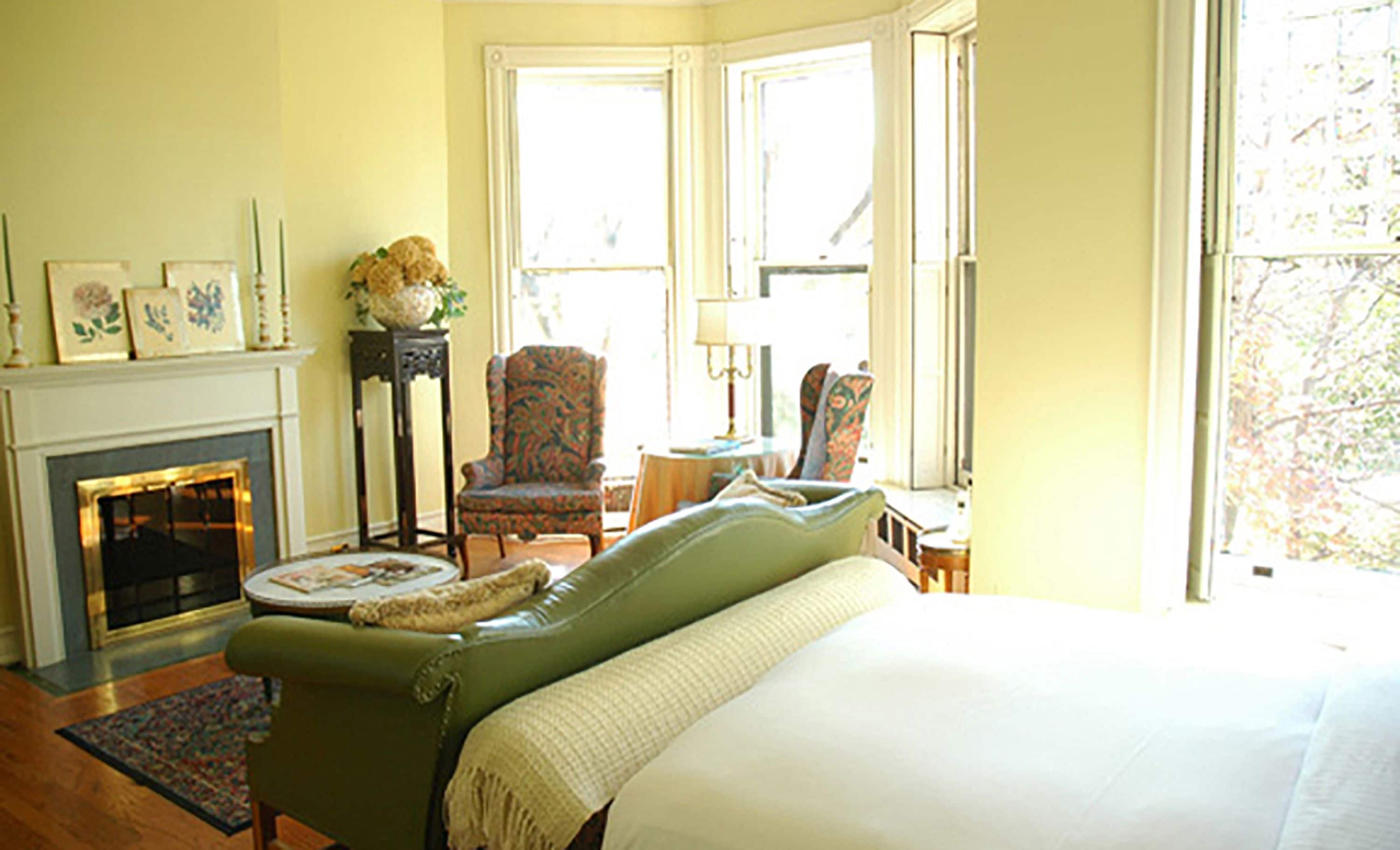 A room with a green armchair, a fireplace, a bed, and a window with a view of trees.