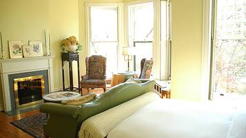 A room with a green armchair, a fireplace, a bed, and a window with a view of trees.