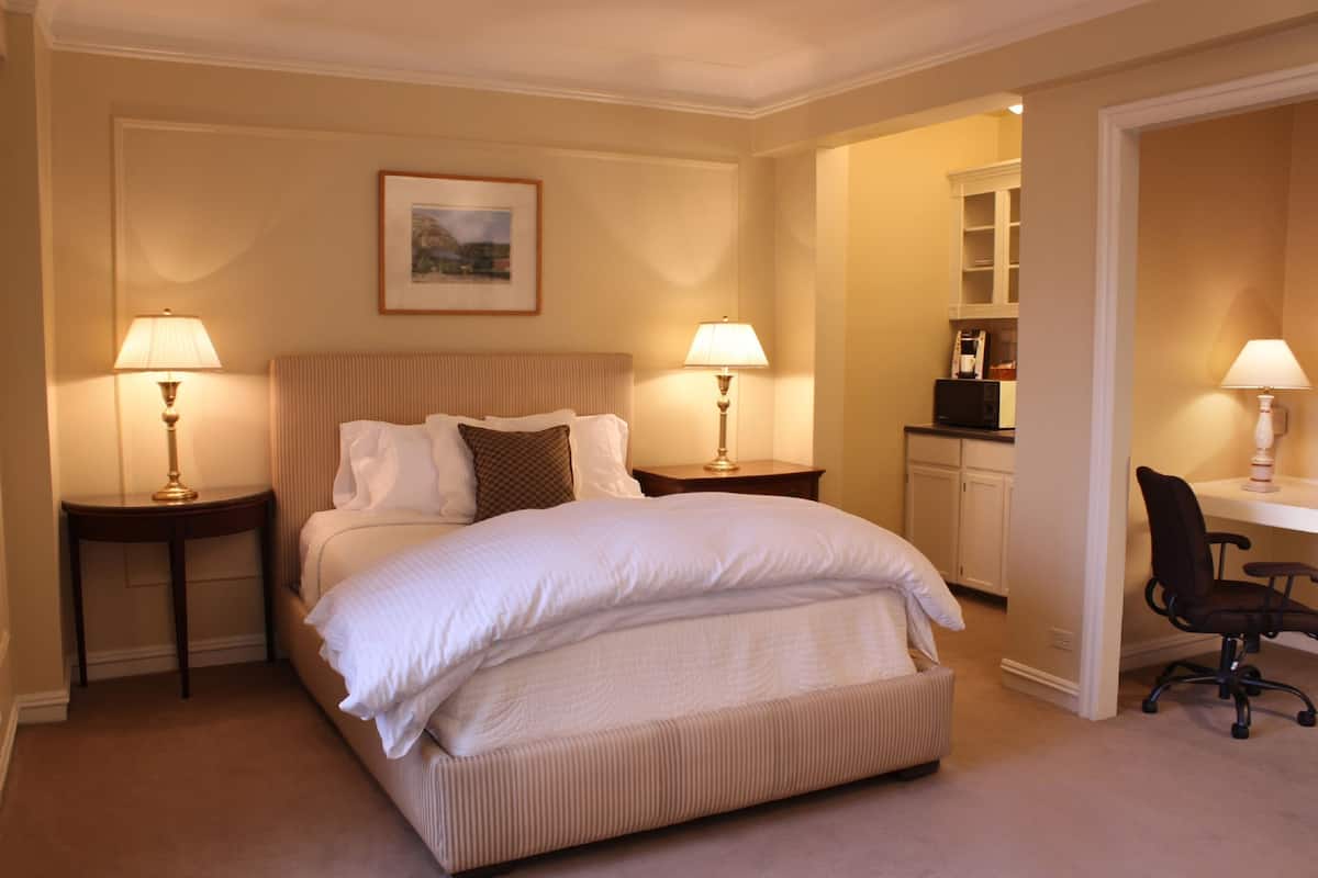 A hotel room with a large bed, two bedside tables with lamps, a desk with a chair, and a wardrobe.