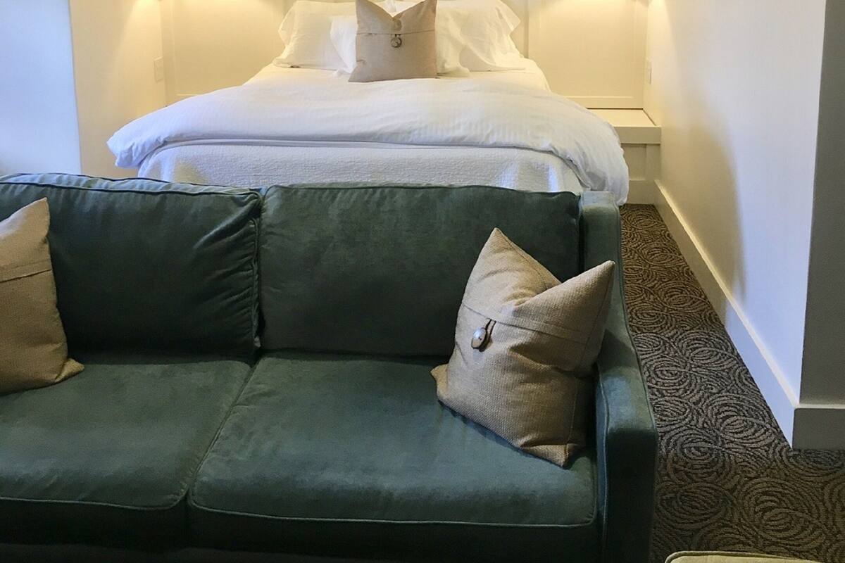 A hotel room with a bed, two wall-mounted lamps, a green sofa, and a patterned carpet.