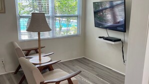 A modern living room with a TV, a lamp, and a pool view. - Venice Beach Villas (Venice)