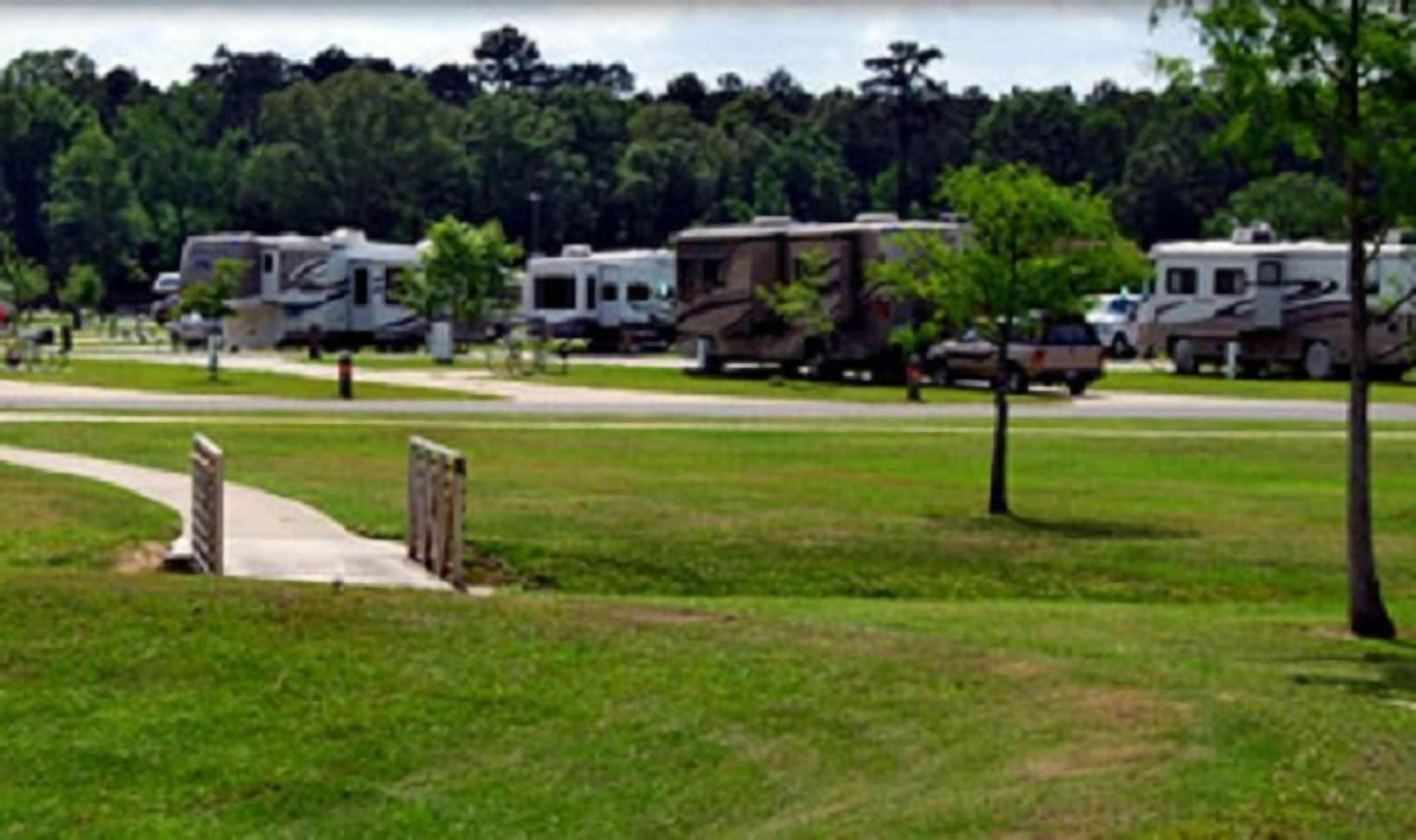 Une rangée de camping-cars est stationnée dans une zone herbeuse, à proximité d’un chemin pavé.