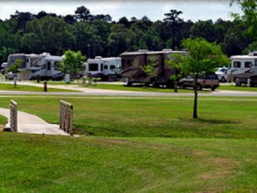 Une rangée de camping-cars est stationnée dans une zone herbeuse, à proximité d’un chemin pavé.