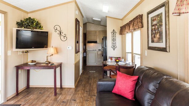 A cozy living room with a leather couch, a TV, and a dining area with a table and chairs. - Red Shoes RV Park (Kinder)