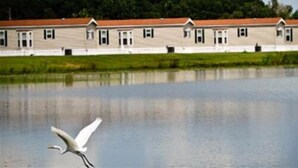 A row of buildings with a reflective water body in the foreground. - Red Shoes RV Park (Kinder)