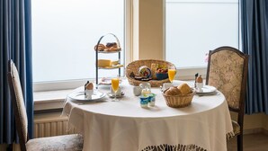Une table à manger dressée avec des aliments pour le petit-déjeuner, un panier de fruits et une vue sur la verdure à l’extérieur.