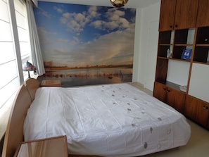 A bedroom with a large bed, a wooden wardrobe, a desk, and a view of a lake through a window. - B&B Villa De Keyser (Eeklo)